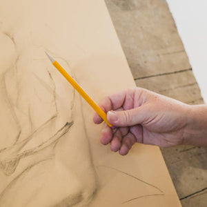 White man's hand making a figue drawing with a yellow mechanical pencil.