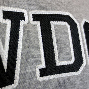 Closeup showing embroidered applique detail of black twill D with white twill outline.