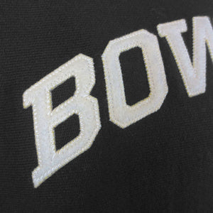 A closeup view of the letters BOW embroidered on the chest of a black sweatshirt, showing the texture of the reverse weave sweatshirt and the quality of the stitching in the ivory thread and felt of the letters.