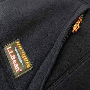A closeup shot of the left pocket of a black fleece jacket, showing the zipper with a bootlace zipper pull, and a colorful L.L.Bean fabric patch sewn on the fleece.