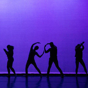 Silhouettes of dancers against a violet purple lit background.