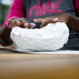 Black woman's hands shaping a white plaster scuplture.