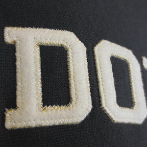 A closeup shot showing the high-quality stitching detail in the ivory felt letters DO on a black reverse weave sweatshirt.