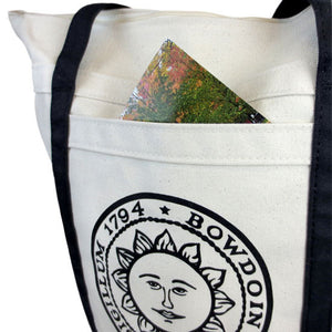 Closeup showing a postcard poking out of the pocket of a Bowdoin seal tote bag.